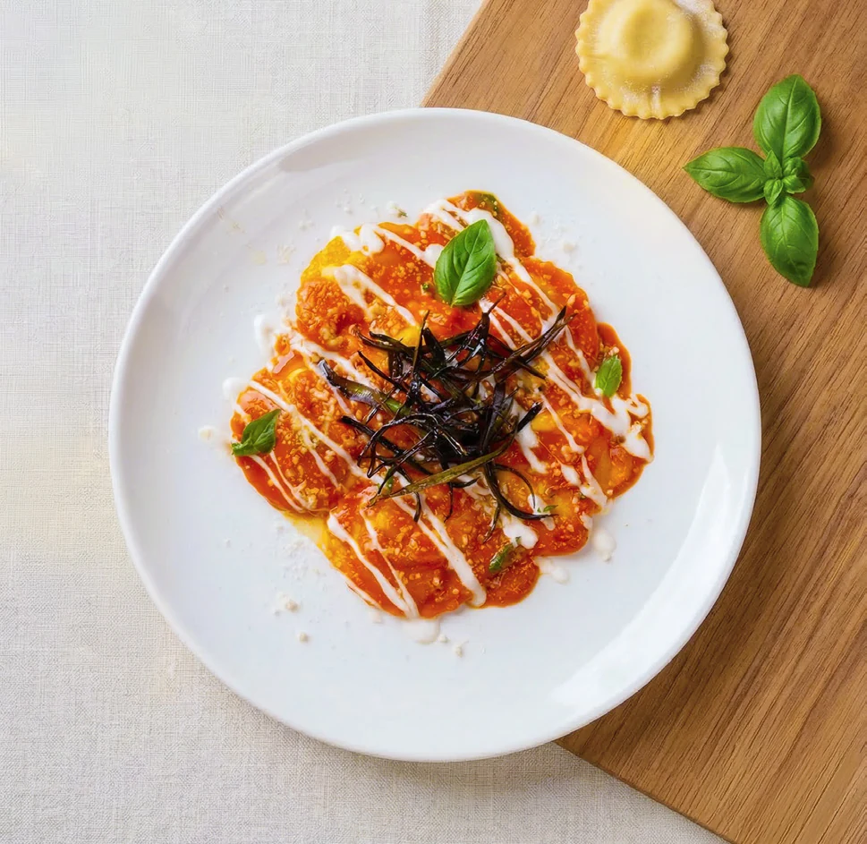 Immagine generata con AI: pasta ripresa dall’alto con basilico e ravioli nella scena.