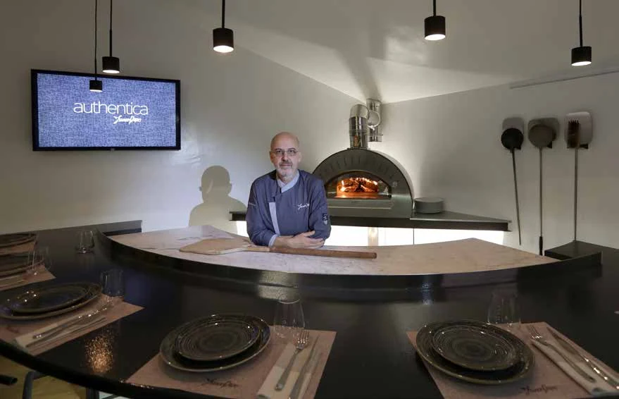 Persona al tavolo, con forno e insegna Authentica sullo sfondo.