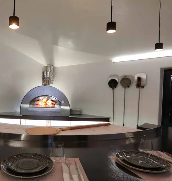 Tavolo apparecchiato davanti a un forno acceso.
