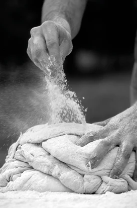 Una mano sparge farina sull’impasto, in bianco e nero.